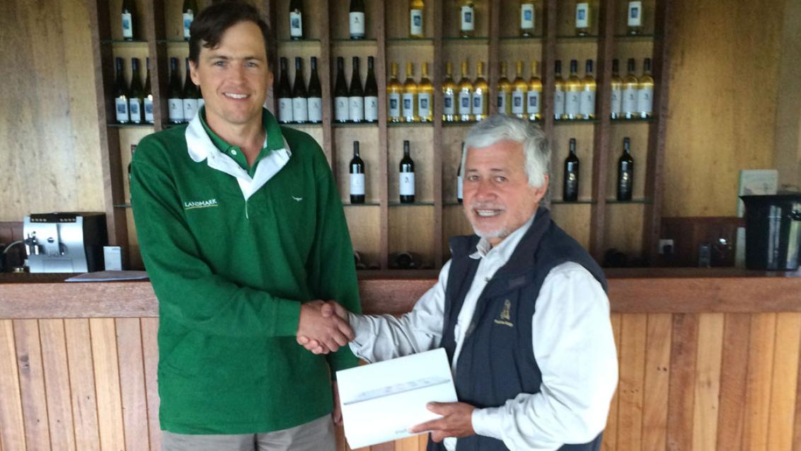 two men shaking hands in front of wine display