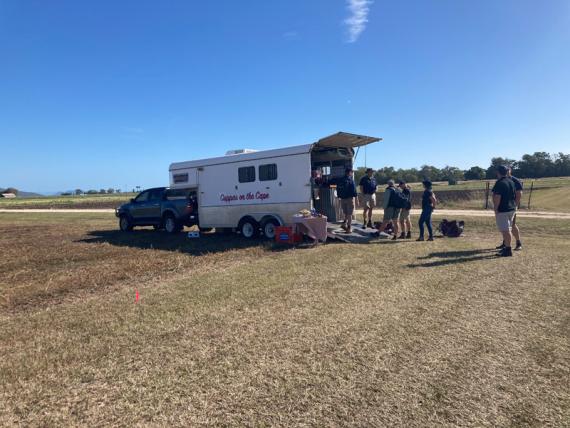 A group of people are gathered around the opened rear of the caravan