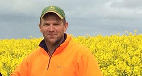 man in hi-vis standing in front of wattle field 